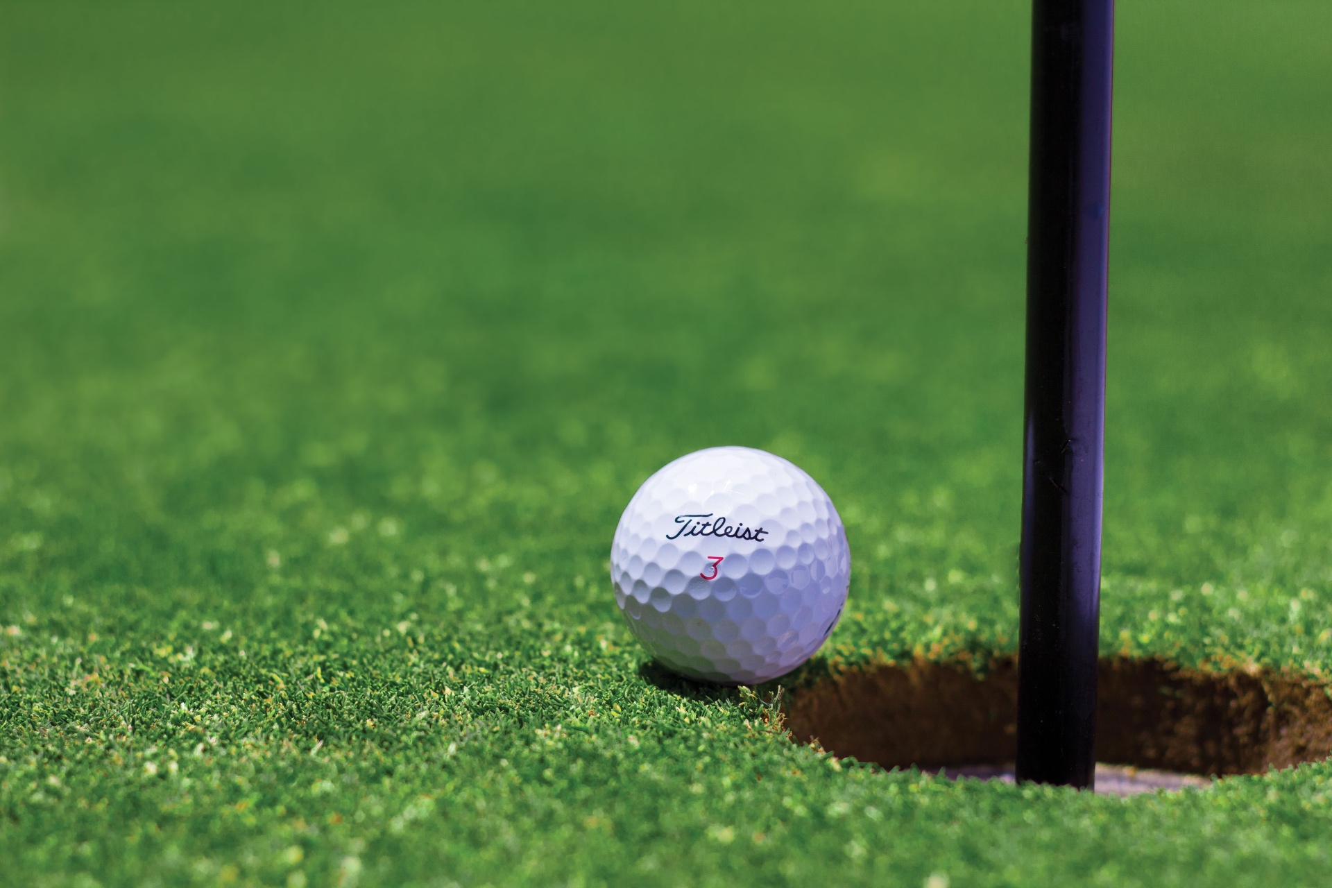 Titleist golf ball resting on the lip of the cup beside the flagstick